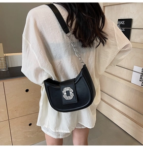 Black crescent shoulder bag with rhinestone buckle worn by a model in a minimal setting
