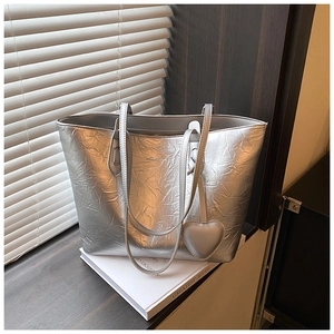 Detail of metallic silver tote bag with crinkled texture and heart-shaped charm pendant