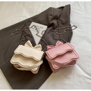 Detail of sweet bow-knot crossbody bags in cream and pink on a gray blazer