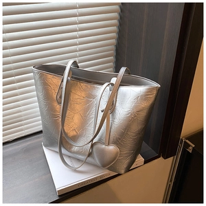 Detail of silver tote bag showing metallic pleated texture and heart charm in natural light