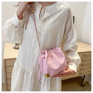 Detailed close-up of pink drawstring bucket bag with gold metal corner protectors and chain