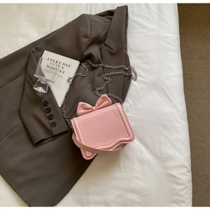 Detail of pink bow crossbody bag with silver chain strap on soft white linens