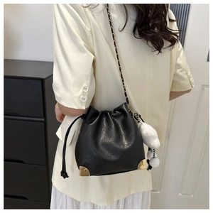 Detail of black drawstring bucket bag with gold metal corners and white plush pom-pom charm