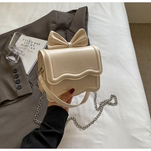 Detailed close-up of cream bow shoulder bag with wavy flap and elegant metal chain