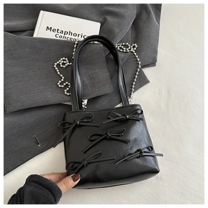 Detail of black bow square bag with silver beaded metal chain on a grey blazer