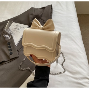 Detail of cream white crossbody bag with wave edge flap and large 3D bow accent