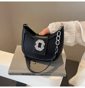 Detail of black crescent leather bag with sparkling crystal buckle on a book