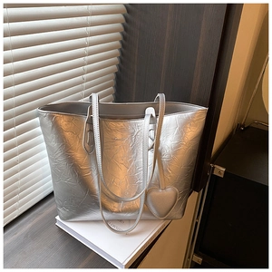 Detail of silver metallic tote bag with crinkled texture and heart-shaped charm accessory
