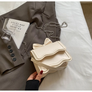 Detail of cream crossbody bag featuring a wavy flap, 3D bow, and silver metal chain strap