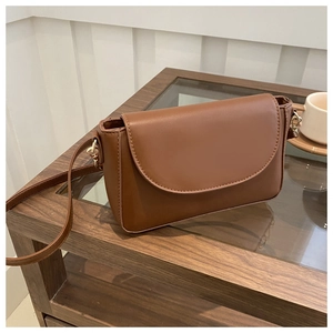 Detail view of a brown faux leather crossbody bag with a gold metal hook on a table