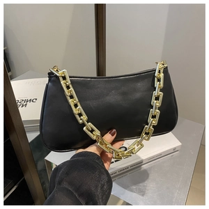 Close-up of black retro baguette bag with chunky gold chain strap on a vintage table