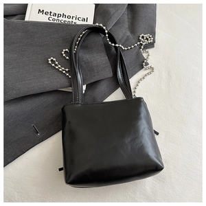 Detail of minimalist black PU leather bag with silver ball chain on a stylish backdrop