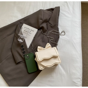Detail view of mini beige crossbody bag with wavy flap and elegant bow accent