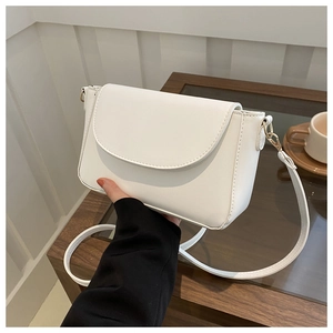 Detail of white PU leather crossbody bag featuring gold hardware and curved flap closure