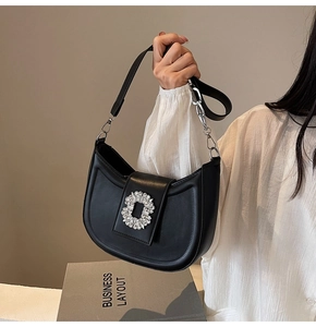 Close-up of black half-moon hobo bag featuring a large crystal buckle and chain strap