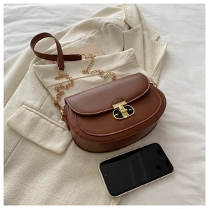 Detail of a brown leather saddle bag with a gold twist-lock and chain strap on a blazer