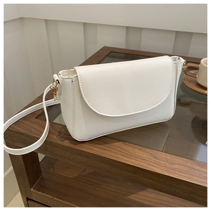 Detailed close-up of a white leather crossbody bag with golden metal hardware on a glass table