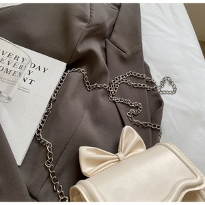Detail of cream crossbody bag with bow accent and chain strap on olive blazer