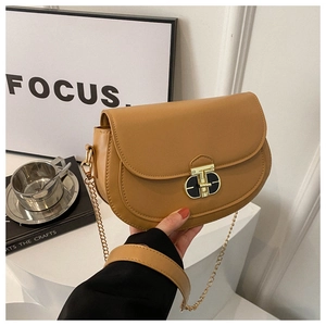 Detail of a brown saddle bag featuring a gold twist lock and chain shoulder strap