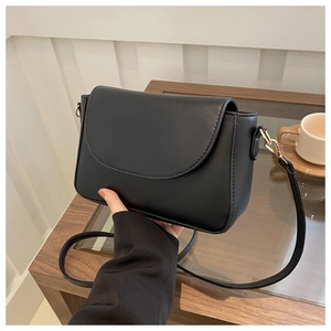 Detail of minimalist black crossbody bag with gold buckle on wooden cafe table