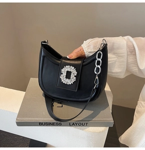 Detail of black leather hobo bag featuring a luxury crystal buckle and silver chain strap