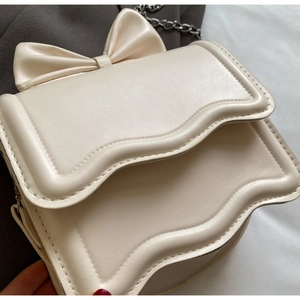 Detail of cream crossbody bag featuring a large bow and wavy edge flap with silver chain