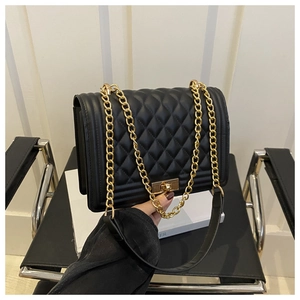 Close-up of black quilted shoulder bag with golden push-lock and metal chain strap