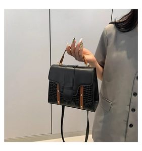Détail du sac en cuir noir crocodile avec poignée marron contrastée et finitions métalliques