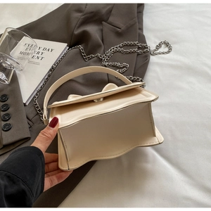 Detail of cream white leather crossbody bag with silver chain strap and magnetic closure
