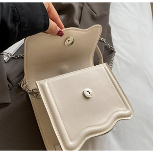 Detail view of cream crossbody bag featuring magnetic closure and silver chain strap