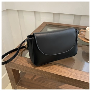 Detail of a minimalist black leather crossbody bag with elegant gold metal hardware accents