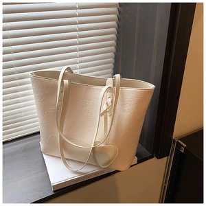 Detail of white tote bag with textured leather, long straps and heart-shaped charm
