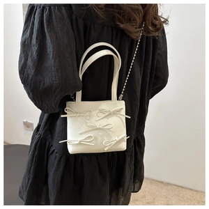 Close-up of cream white handbag with 3D bow details and delicate metal ball chain