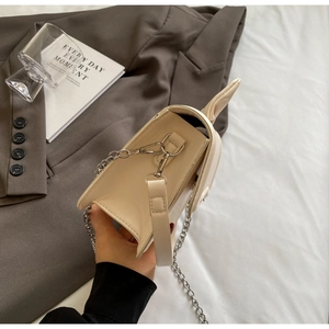 Close-up of a beige crossbody bag featuring a silver chain strap and leather shoulder pad