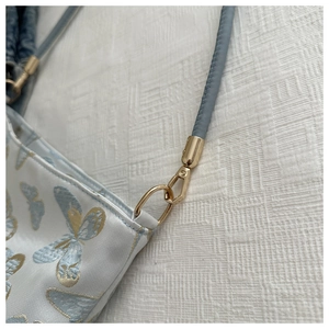 Detailaufnahme der goldenen Hardware und feinen Stickerei auf einer blauen Handtasche