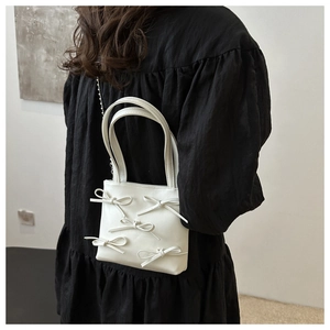 Detail of white mini tote bag with ribbon bows and dual handles on black dress