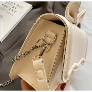 Detailed shot of beige leather crossbody bag with silver chain hook and bow design