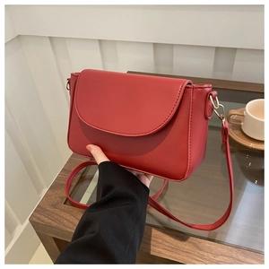 Detail of red matte leather crossbody bag with gold hardware held in an elegant cafe setting
