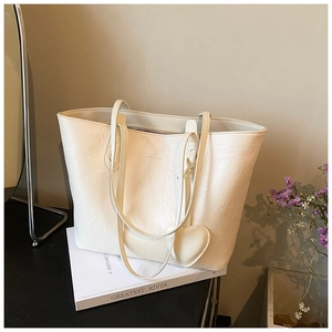 Detail of cream tote bag with crinkled texture, slender straps, and heart pendant accessory