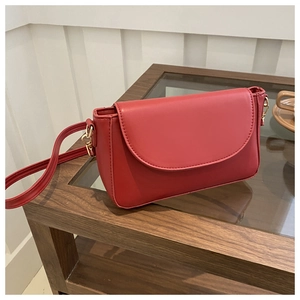 Detail view of a stylish red rectangle shoulder bag on a glass table in a lifestyle setting