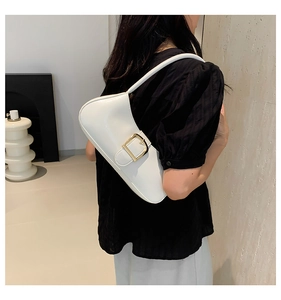 Detail of white baguette bag with large gold buckle against a minimal interior