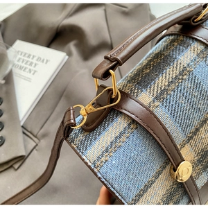 Detail of blue and beige checkered fabric bag with brown leather handle and gold hardware