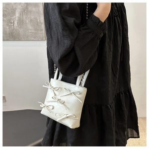 Detail of white mini bow handbag with silver ball chain strap on a black dress