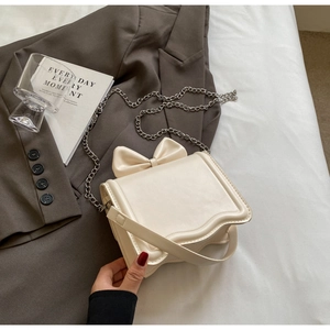 Detail of cream crossbody bag featuring a 3D bow decor and unique wavy bottom edge