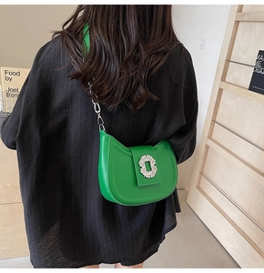 Detail view of a green leather saddle bag with a luxury rhinestone buckle and chain strap