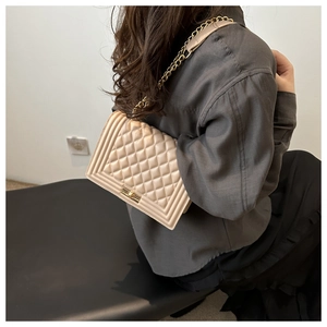 Detail of a beige quilted chain bag with a rectangular metal push-lock and stylish chain strap