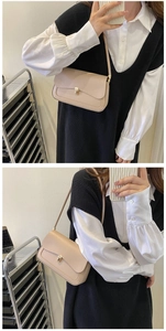 Close-up of beige leather shoulder bag featuring a gold rectangular metal clasp and minimalist flap