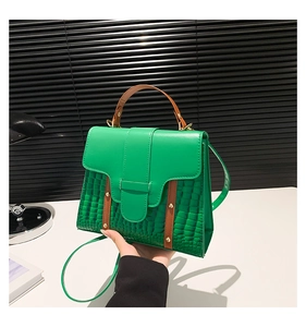 Detail of green faux leather handbag with crocodile pattern and brown decorative straps