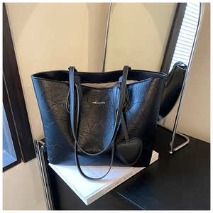 Detail of a black pleated tote bag with silver logo and leather heart pendant accessory