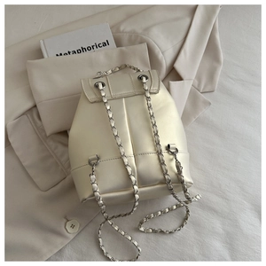 Detailed close-up of cream-white leather backpack with metallic chain straps and matte finish